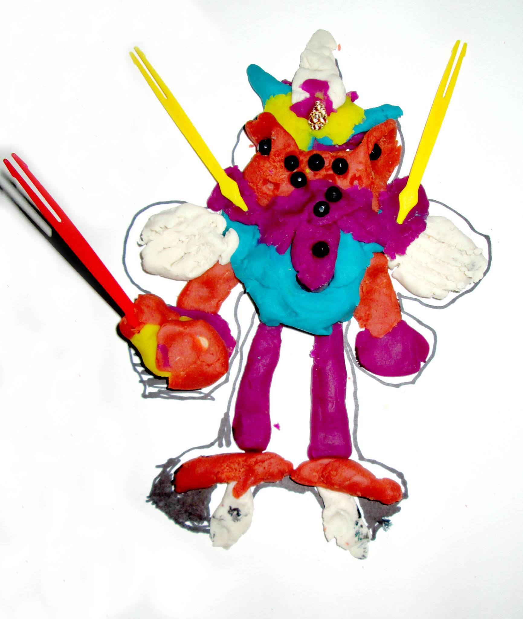 A child's brightly colored modeling-clay monster sculpted over their own outline drawing, with plastic-fork antennae and small beads pressed into its chest