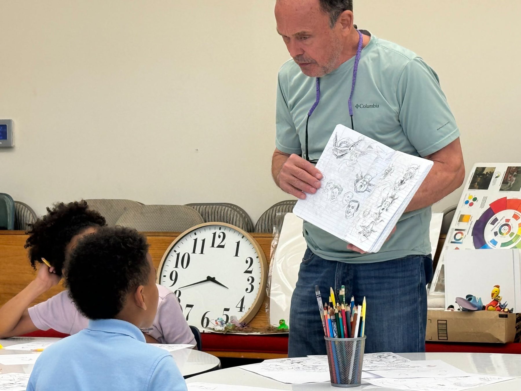 Eric showing a sketchbook of character studies to a young student in class