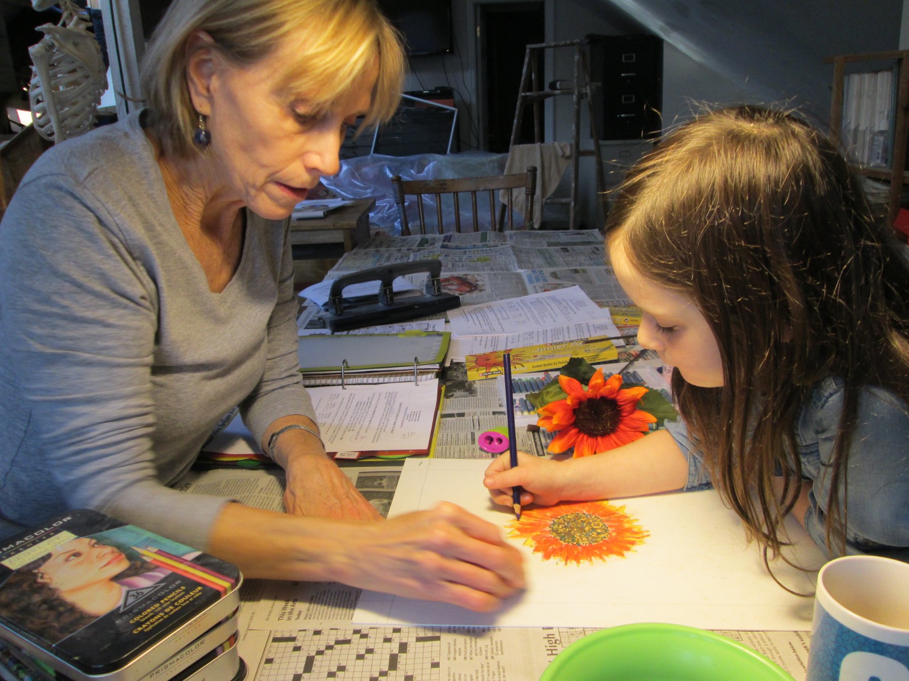 Dianne guiding a young student drawing a sunflower in colored pencil