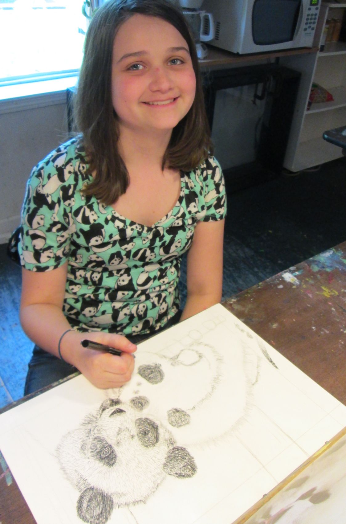 A young student smiling while working on a detailed pen-and-ink panda drawing